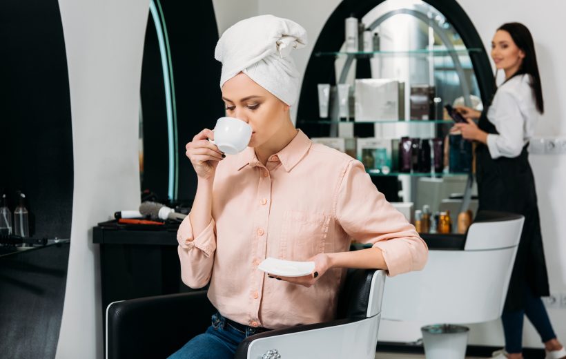 customer with towel on head sitting and drinking coffee in hair salon